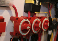 Three red battery switches installed on a white marine panel with red cabling