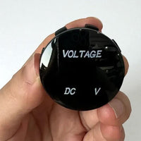 Person holding the small round voltmeter gauge to demonstrate compact size