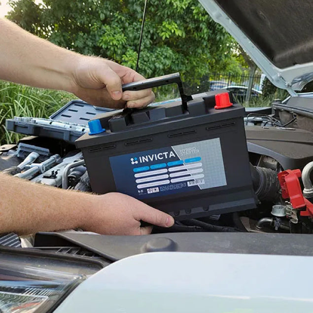Mechanic lowering lightweight Invicta lithium battery into engine bay by handle