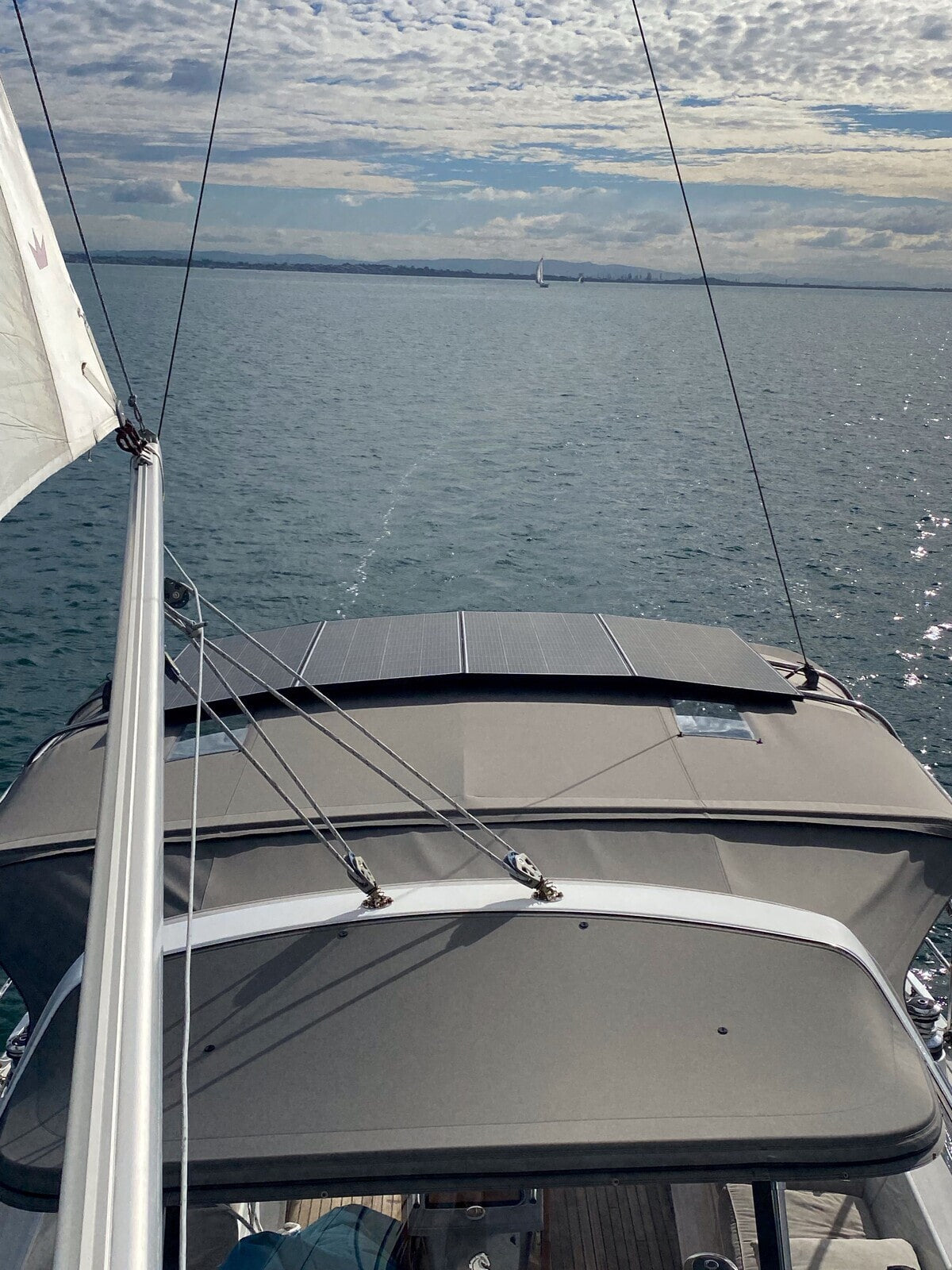 Three fixed solar panels mounted on the grey canvas bimini top of a sailboat moving through water