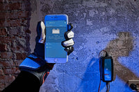 Gloved hand holding a phone showing the Victron app interface with charger mounted on wall