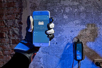 Person in workshop using a smartphone to monitor a wall-mounted Victron Blue Smart charger