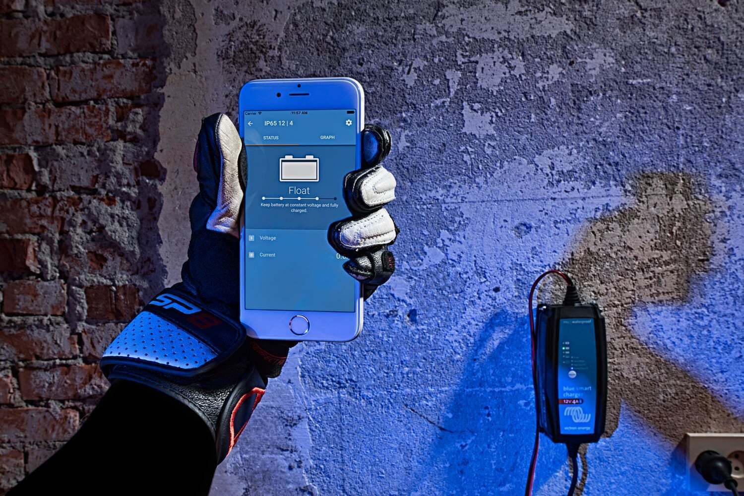 Smartphone displaying charging status in the VictronConnect app held by a person in motorcycle gear