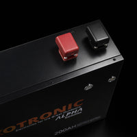 High-angle close-up of red and black M8 battery terminals with protective covers on top of black metal casing