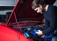Man using VictronConnect app on a smartphone to monitor a battery charger in a car engine bay