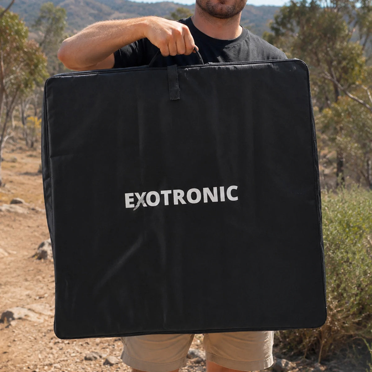 Man carrying the folded 200W solar panel in its bag through an outdoor bush setting